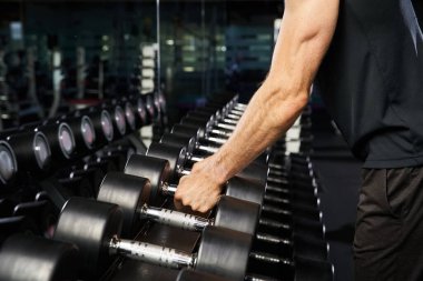 Aktif giyinen bir adam spor salonunda bir çift dambılı kavrayıp forma ve dayanıklılık eğitimine olan bağlılığını gösterir..