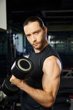 Aktif kıyafetli bir adam spor salonunda bir dambıl tutuyor, atletizmini ve spora olan bağlılığını gösteriyor..