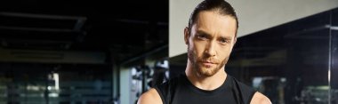 Aktif giyinmiş bir adam spor salonunda aynanın önünde duruyor, vücut ve kaslarını inceliyor..