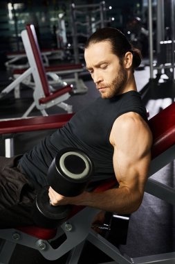 Aktif giyinen atletik bir adam spor salonunda çalışırken elinde bir çift dambıl ile bankta oturur..