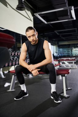 Spor kıyafetli bir sporcu spor salonunda oturuyor, hareketli antrenmanlarına ara veriyor..