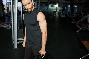 Atletik bir adam spor salonunda siyah bir tabak tutuyor..