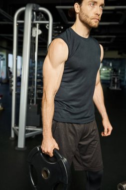 Spor salonunda dambılı kaldıran, spor yaparken güç ve kararlılık gösteren etkin bir sporcu..