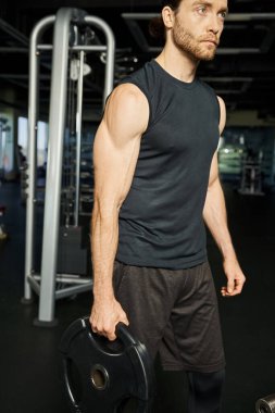 An athletic man in active wear lifting a dumbbell in a gym, showcasing strength and determination in his workout routine. clipart