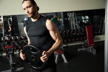 Atletik bir adam spor salonunda siyah bir tabak tutuyor..
