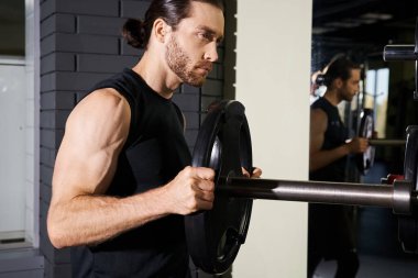 Aktif giyinmiş kararlı bir adam, bir halteri kavrar, gücünü ve bağlılığını bir spor salonunda gösterir..