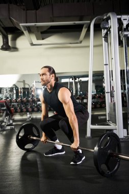 Aktif çalışan bir adam spor salonunda halterle çömelir..