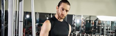 Siyah kolsuz tişörtlü formda bir adam iyi donanımlı bir spor salonunda egzersiz yapıyor. Güç ve dayanıklılık eğitimine odaklanıyor..