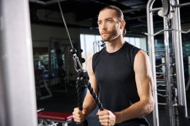 Aktif giyinen atletik bir adam spor salonunda bir ip tutuyor. Antrenmanında güç ve kararlılık gösteriyor..
