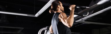 Aktif giyinen atletik bir adam spor salonundaki barfiks barında egzersiz yapıyor..