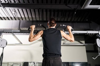 Spor salonunda, spor kıyafeti giymiş bir adam antrenman sırasında ağırlık kaldırıyor..