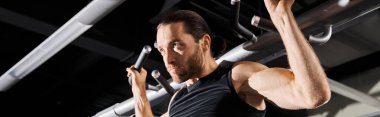 Aktif kıyafetli bir adam spor salonundaki barfiks çekerek fiziksel gücünü ve kararlılığını gösteriyor..