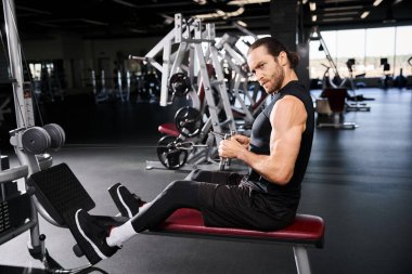 Spor kıyafetleri içinde odaklanmış bir adam spor salonundaki bir bankta derin derin oturur..