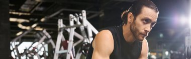Siyah kolsuz tişörtlü atletik bir adam spor salonunda çömelme egzersizi yapıyor. Güç toplamaya ve kaslarını geliştirmeye odaklanıyor..
