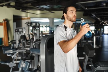 Aktif giyimli bir sporcu spor salonunda çalışırken biberondan su içmek için mola verir..