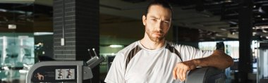 Spor salonundaki bir makinenin yanında duran formalı bir adam..