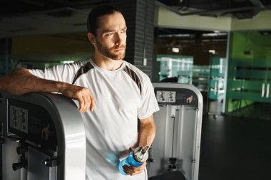 An athletic man in active wear standing confidently next to a gym machine. clipart