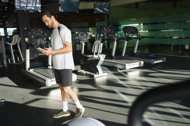 Spor salonundaki antrenmanına ara verirken cep telefonunu kontrol eden kaslı bir adam..