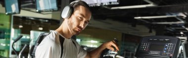 Aktif giyinen atletik bir adam müzik geliştirme seansı için kulaklık takarken makine kullanıyor..