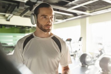 Atletik bir adam spor salonunda çalışırken kulaklıkla müzik dinler..
