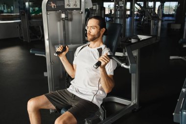 An athletic man in active wear sits on a bench in a gym, pausing between sets with a focused expression. clipart
