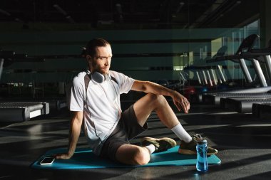 Aktif giyimli formalı bir adam bir mindere oturmuş kulaklık takıyor..