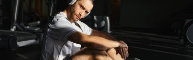 Aktif giyinen atletik bir adam spor salonunda oturur ve yoğun çalışma rutininin ortasında biraz dinlenir..