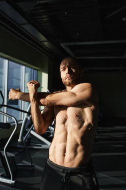Üstsüz, kaslı bir adam spor salonunda kaslarını esnetir. Gücünü ve fiziksel hünerini gösterir..