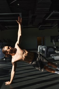 Kaslı bir adam, üstsüz, spor salonunda amuda kalkarak güç ve denge gösterisi yapıyor..