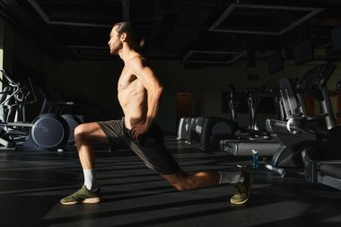 Spor salonunda çömelme hareketleri yapan kaslı bir adam..