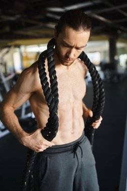 Spor salonunda spor yaparken boynuna ve vücuduna ip bağlayan üstsüz kaslı bir adam..