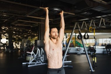 Gömleği olmayan kaslı bir adam spor salonunda barfiks çekiyor..