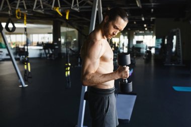Spor salonunda spor aletlerini tutarken kaslı vücudunu sergileyen üstsüz bir adam..