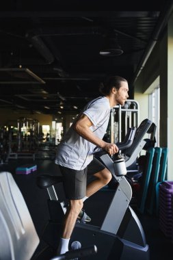 Muscular man pushing his limits, sprinting on a stationary bike in a modern gym environment. clipart