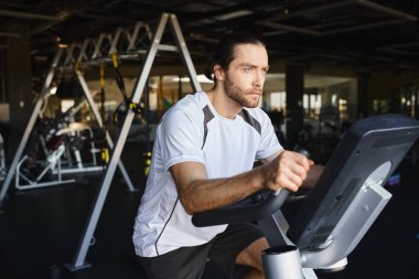 Spor salonunda bisiklete binen kaslı bir adam formda ve dayanıklı olmaya odaklanıyor..