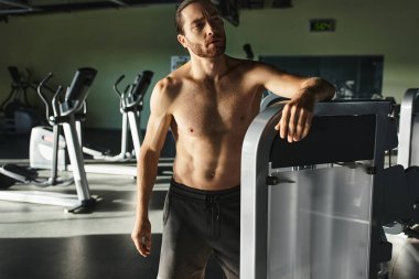 Spor salonundaki büyük makinenin yanında kaslı adam egzersiz yapıyor..