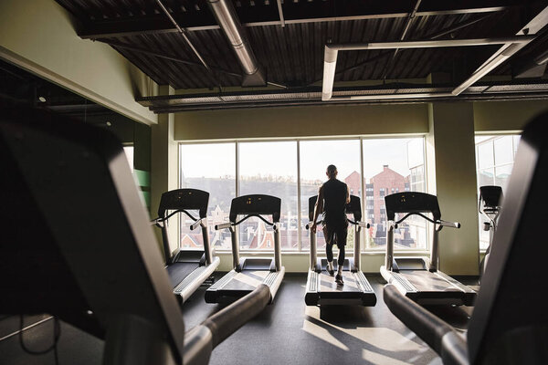 An athletic man in active wear stands on a treadmill in a gym, focusing on his workout routine.
