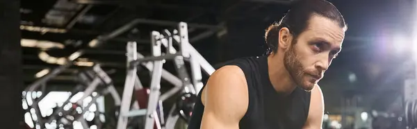 Stock image An athletic man in a black tank top is performing a squat exercise in a gym, focusing on building strength and toning muscles.