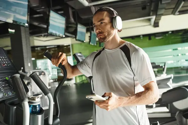 穿着运动服在跑步机上慢跑 同时通过耳机沉浸在音乐中的活跃男子 — 图库照片