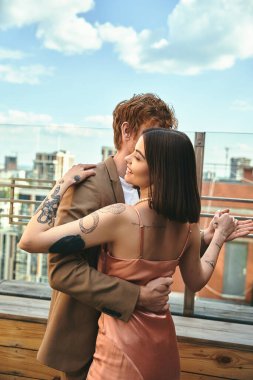 A man and a woman stand embracing on a rooftop at sunset, their silhouettes outlined against the colorful sky clipart