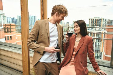 A sophisticated man and woman stand together, the woman holding a glass of wine, embodying grace and class clipart