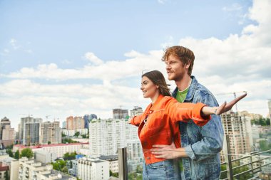 A man and a woman stand confidently on the rooftop of a building, overlooking the cityscape below, their hair blowing in the wind clipart