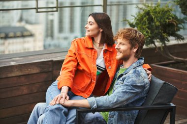 Bir adam ve bir kadın, parktaki ahşap bir bankta yan yana oturuyorlar, birbirlerine eşlik ederek eğleniyorlar.