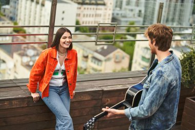 Bir erkek bir kadının yanında gitar çalar, açık havada güneşli bir günde uyumlu bir müzik performansı yaratır.