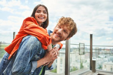 A brave man holds a woman while standing on the edge of a tall building, overlooking the city below, showcasing love and trust clipart