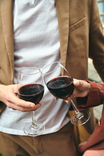 A stylish man with a glass in each hand filled with red wine, showcasing elegance and sophistication