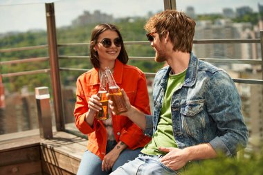 Bir adam ve bir kadın, huzurlu bir ortamda huzurlu bir anı paylaşırken, bir bankta oturup biranın tadını çıkarıyorlar.