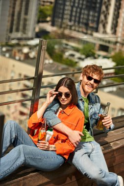 A man and woman are comfortably seated on top of a wooden bench outdoors, enjoying each others company clipart