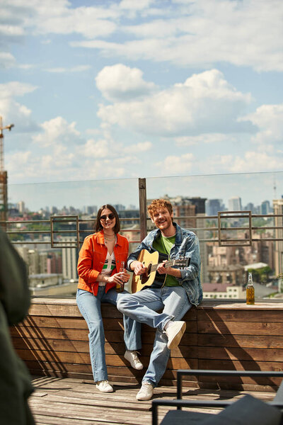 A man and a woman sit on a bench, strumming guitars in sync, creating a harmonious melody in a serene setting