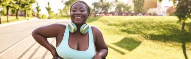 Kıvrımlı bir vücudu olan, mavi bir bluzu ve kulaklığı olan, açık havada müziği seven şık bir Afrikalı Amerikalı kadın..